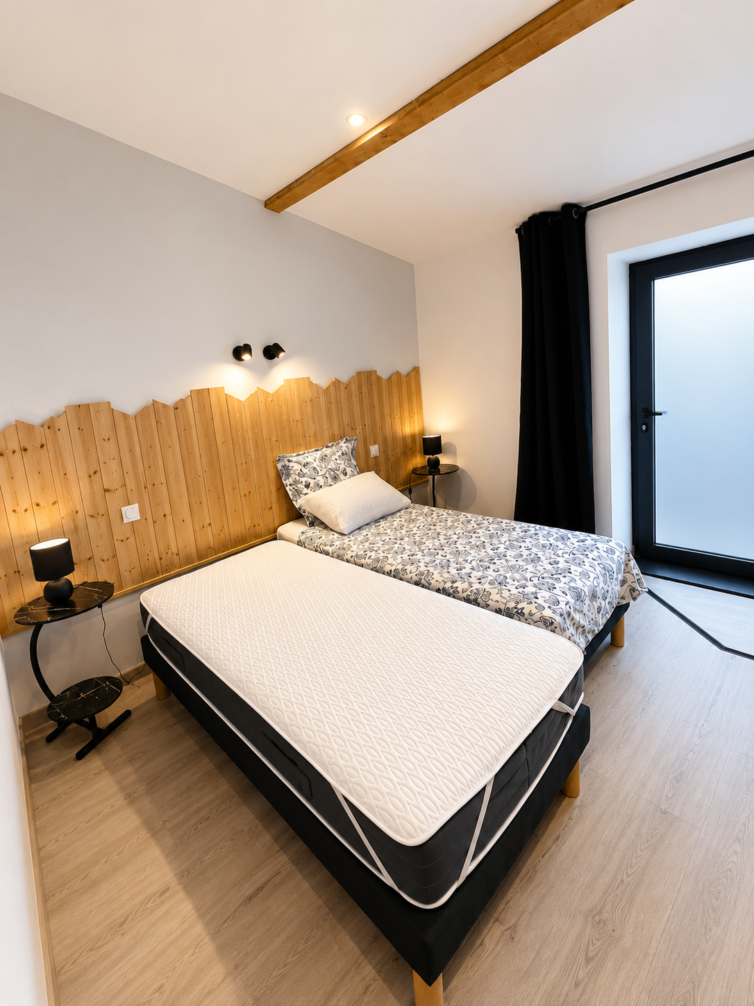 Chambre lumineuse avec tête de lit en bois et grande baie vitrée — Gîte du Pilat